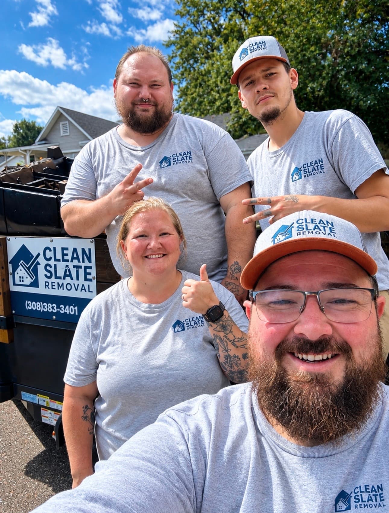 Smiling Clean Slate Removal team members posing for a selfie in front of a company trailer.