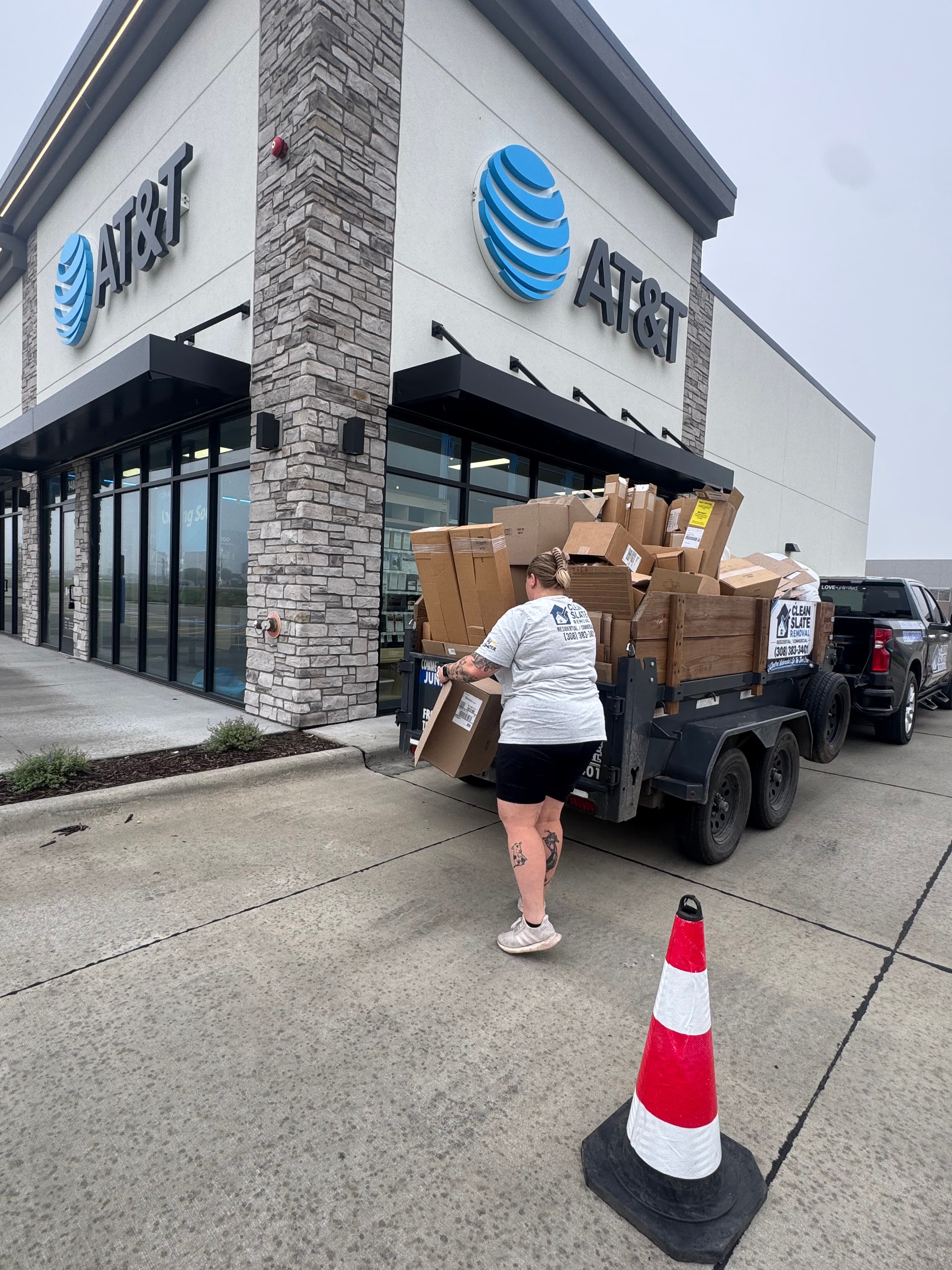 Woman loading cardboard boxes into a trailer parked in front of an AT&T store.