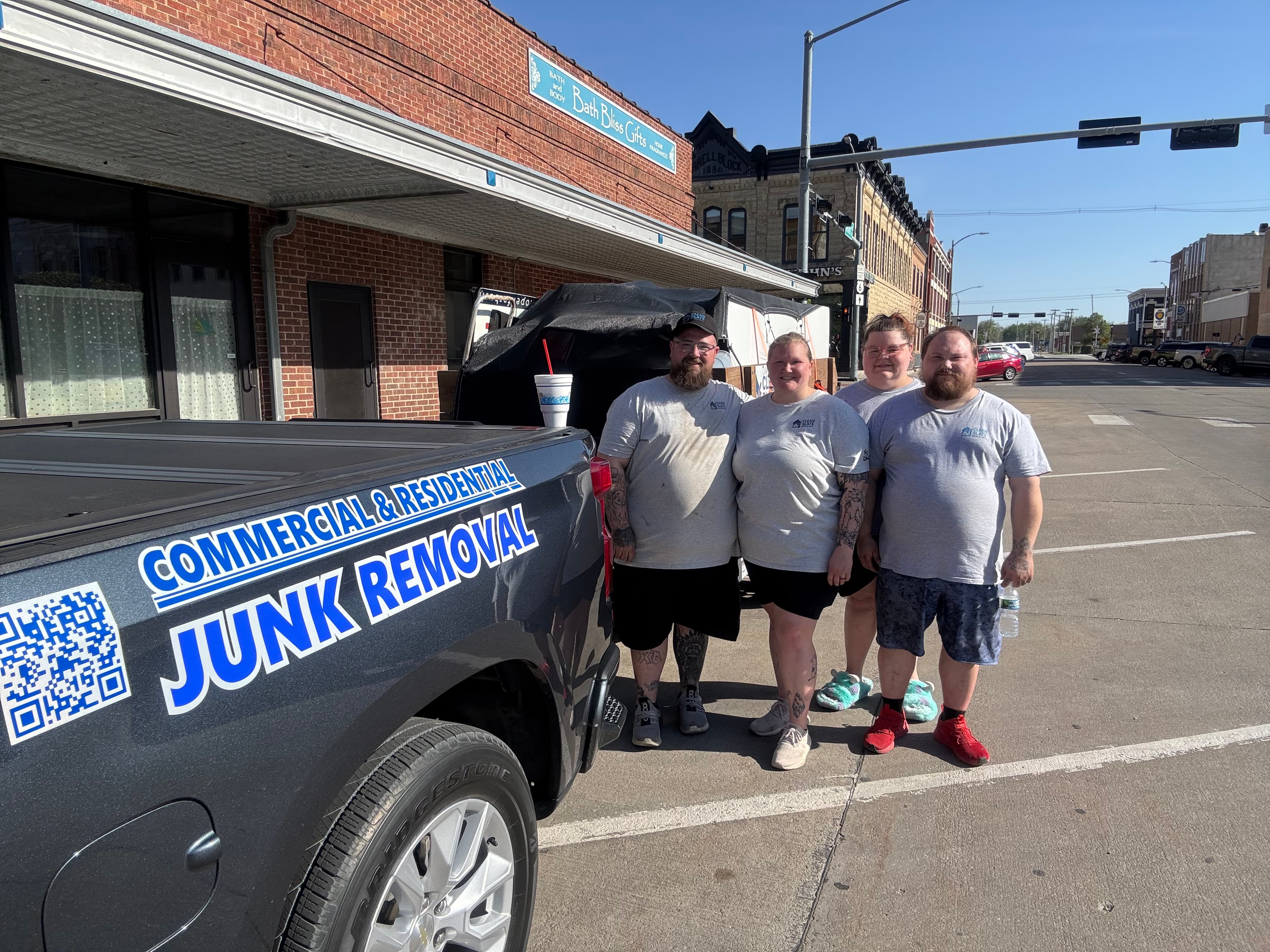 Four workers in matching grey shirts pose beside their commercial and residential junk removal truck.