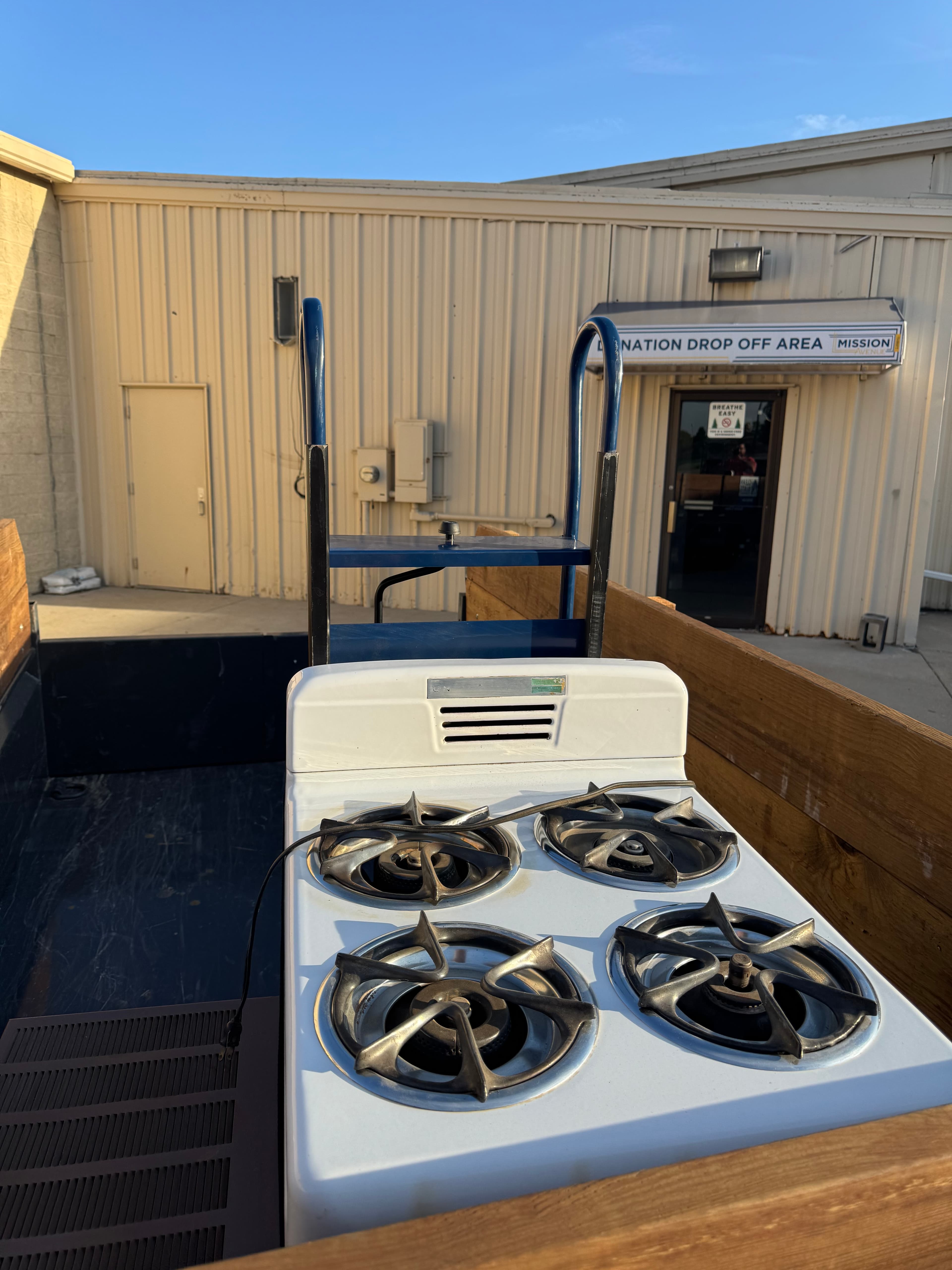 White vintage gas stove in a wooden truck bed outside a donation drop-off center.