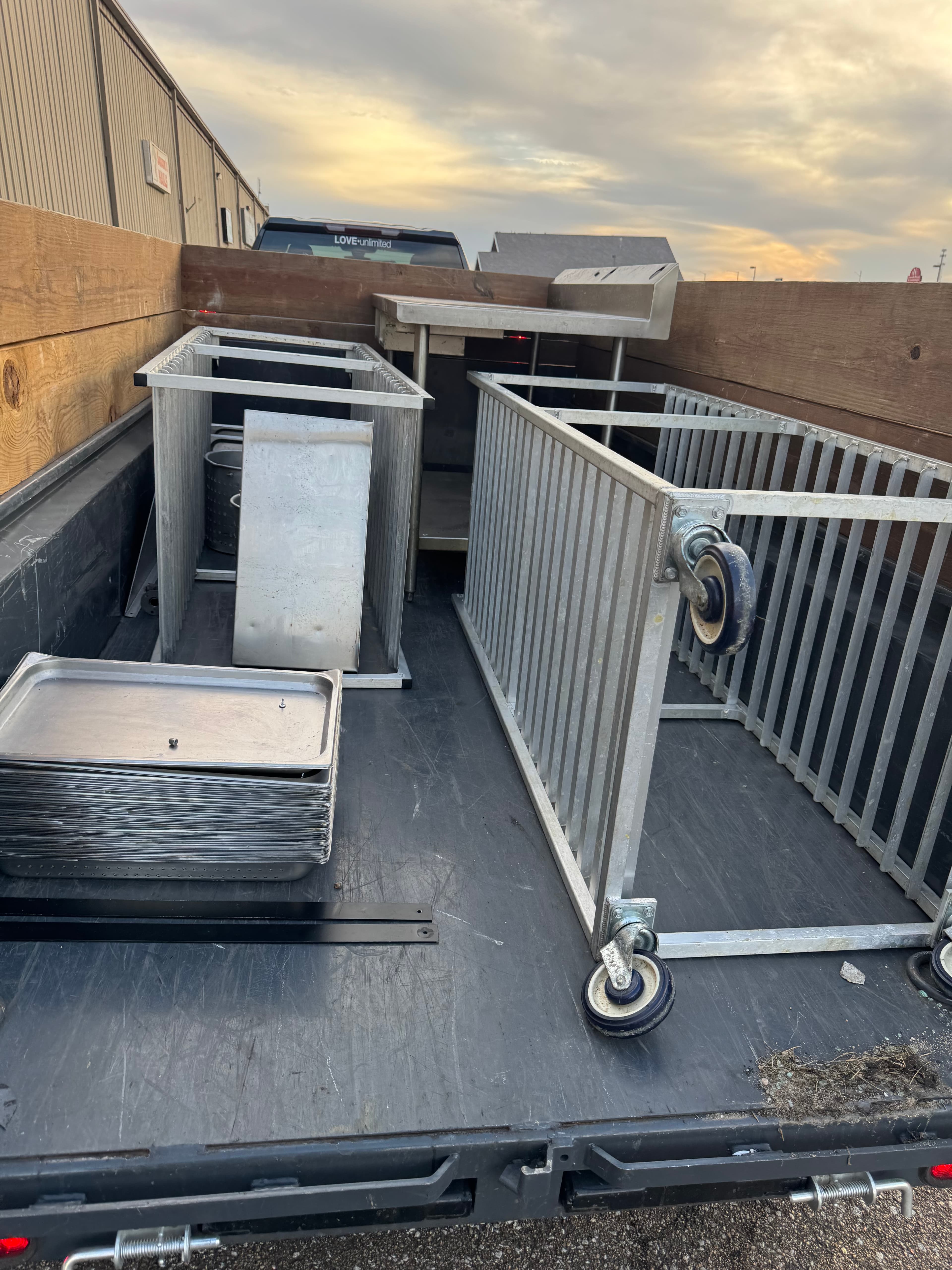 Metal kitchen racks, a prep table, and stacked trays in a truck bed.