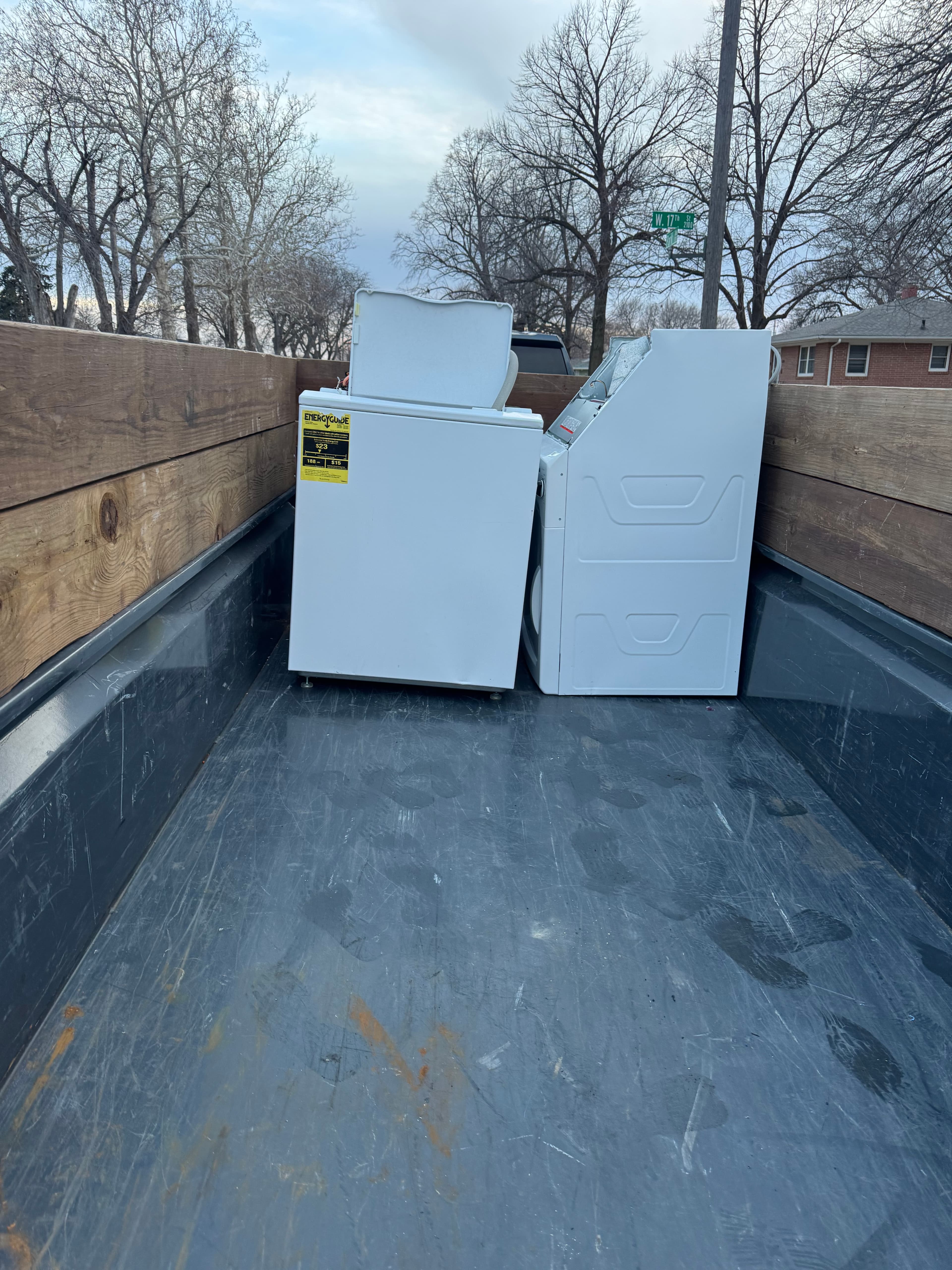 White washing machine and dryer loaded in a truck bed with wooden side rails.