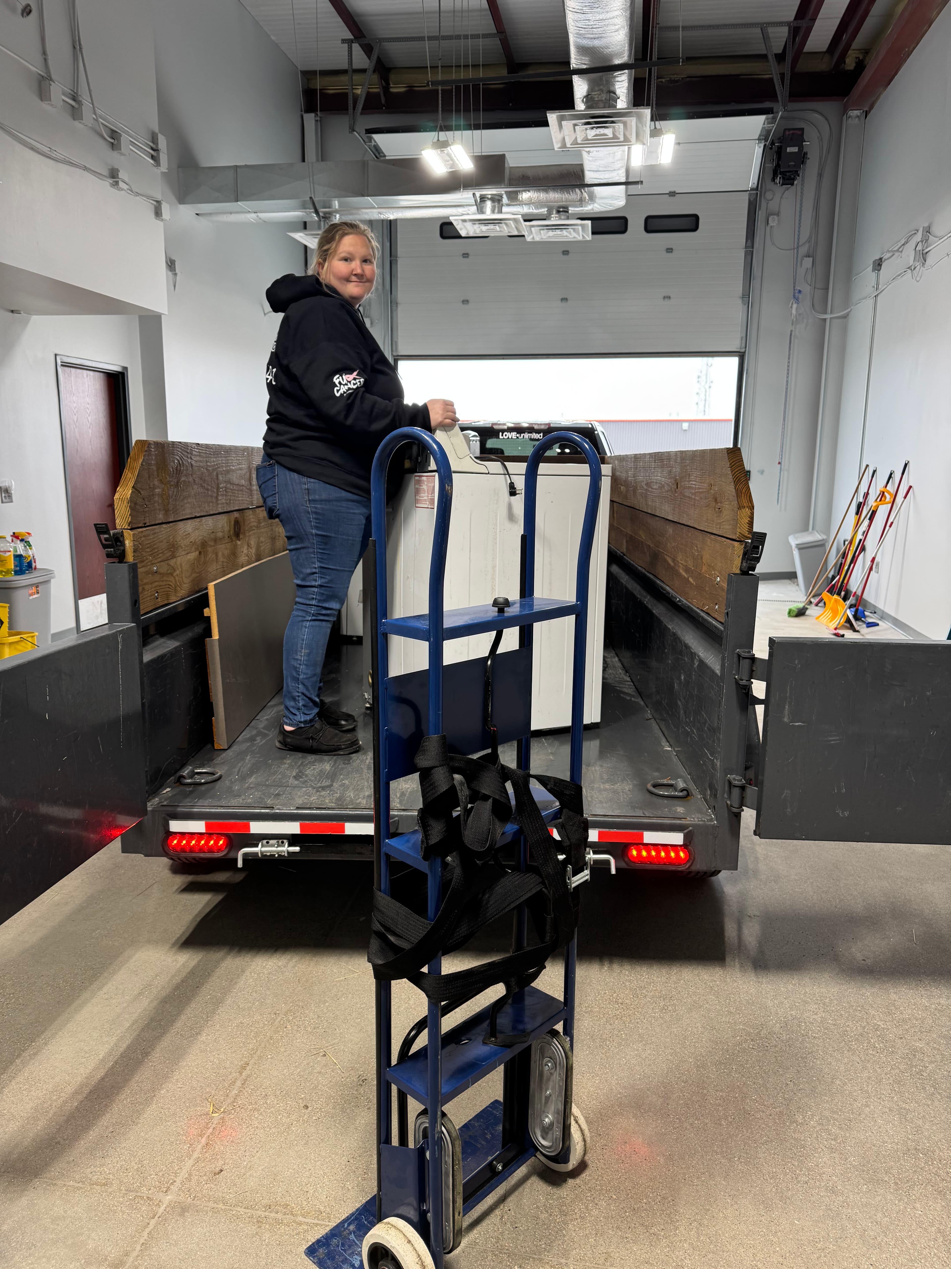 Woman loading a white appliance into a trailer with a blue hand truck.