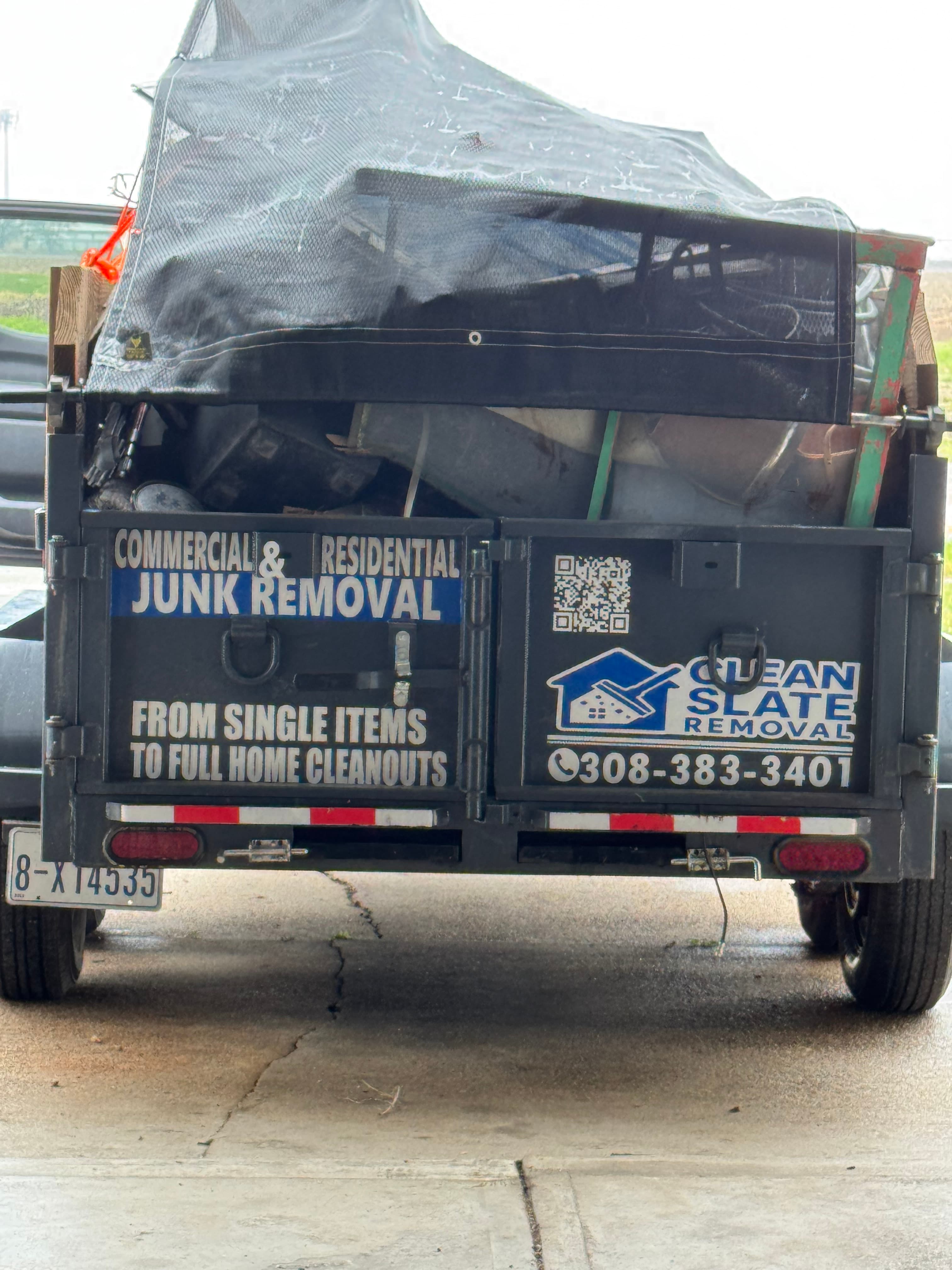 Black trailer filled with junk, featuring Clean Slate Removal branding and a phone number.