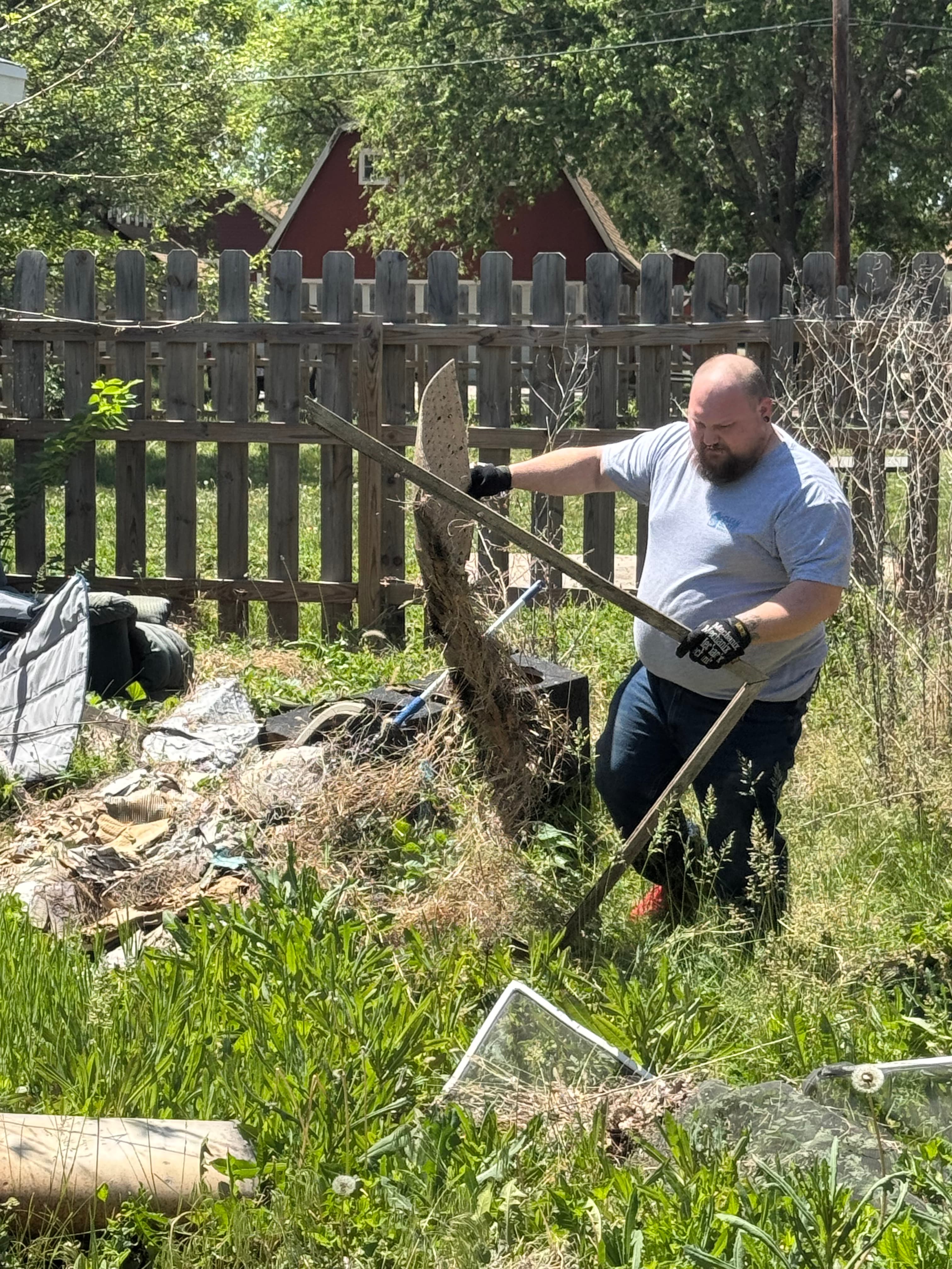 Bearded man in a grey shirt lifts a wooden frame from a pile of debris.