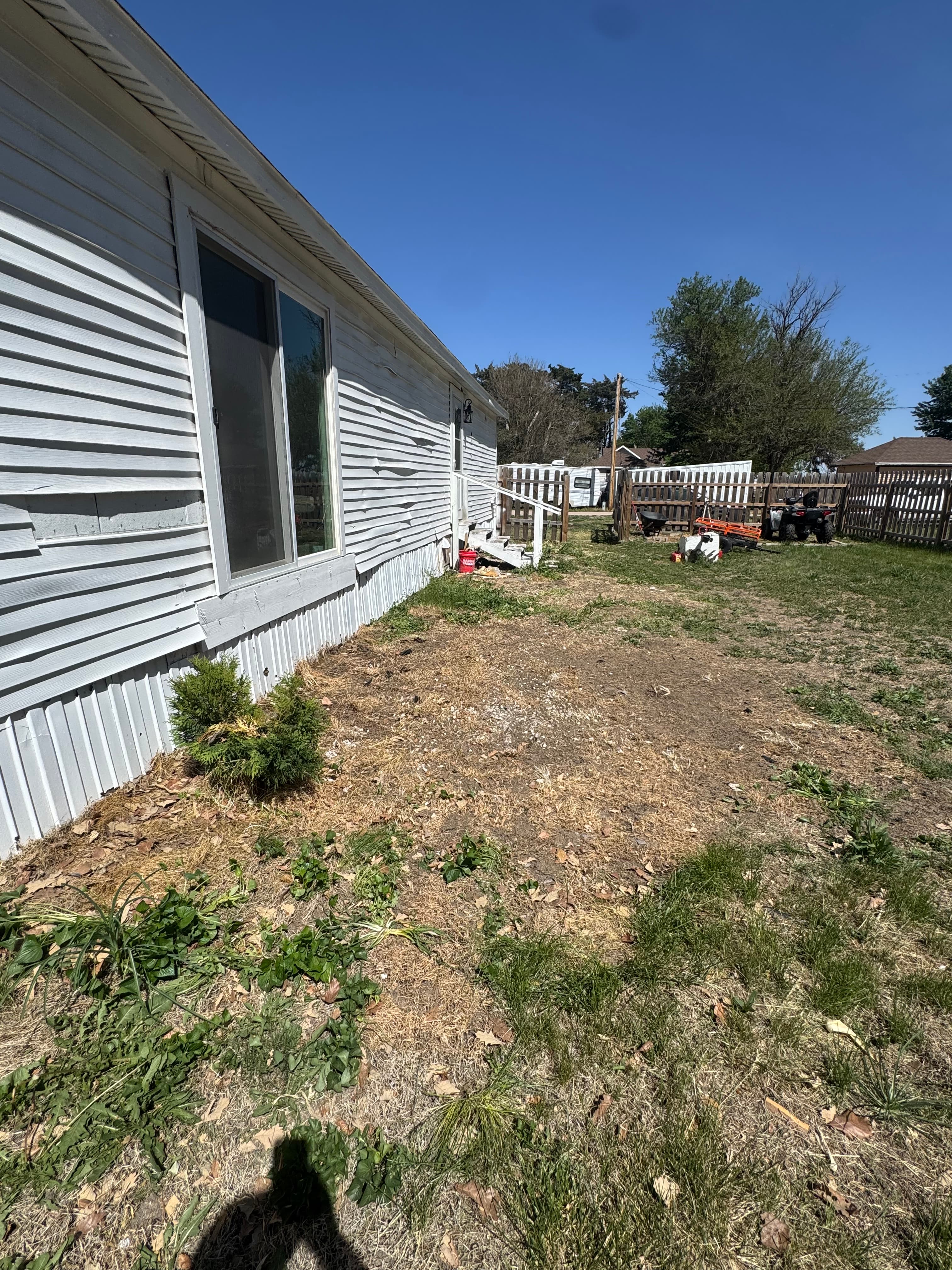 White house with warped siding and a dry, unkempt yard under a blue sky.