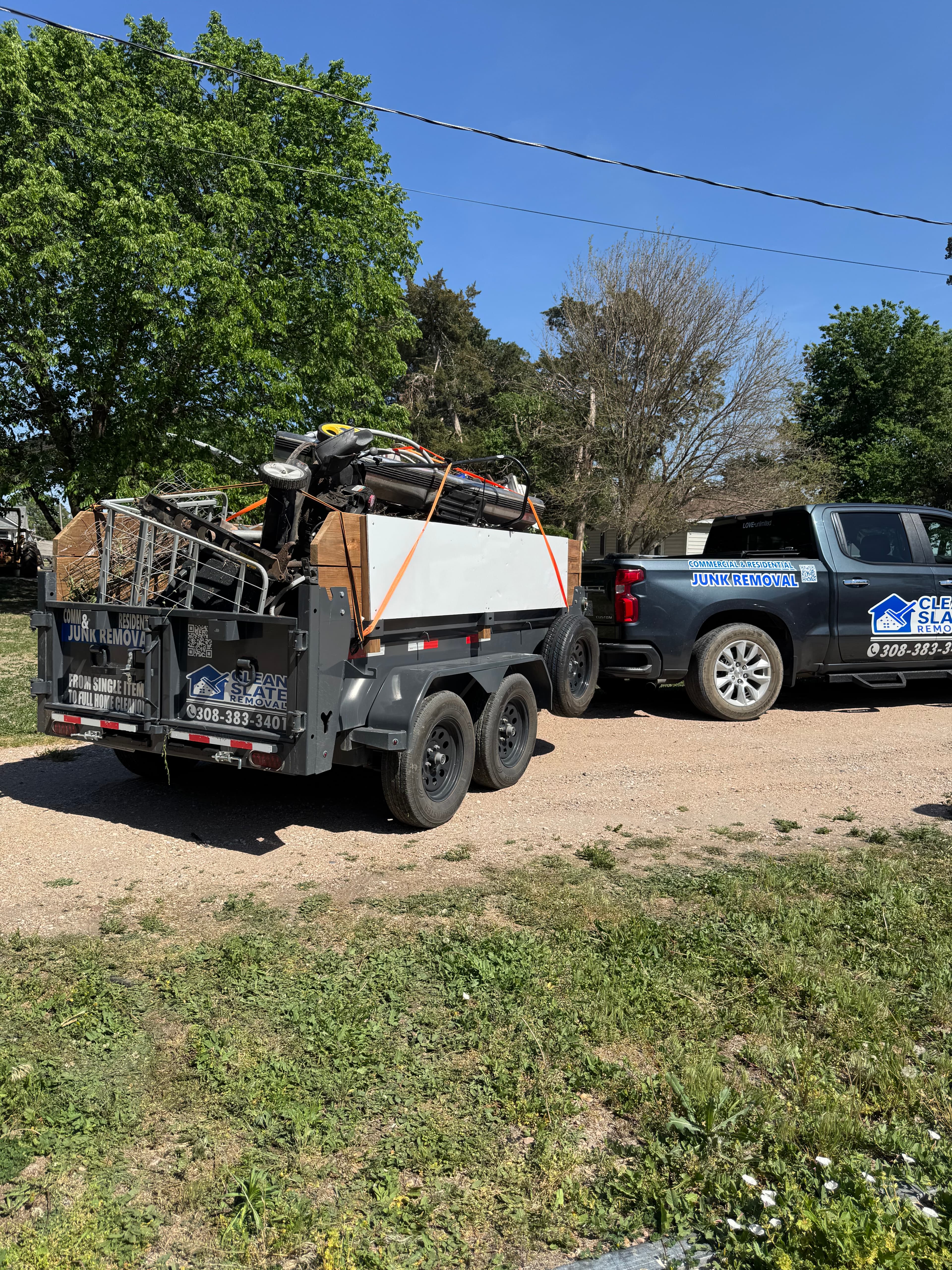 Dark gray junk removal truck towing a trailer overflowing with metal debris and equipment.