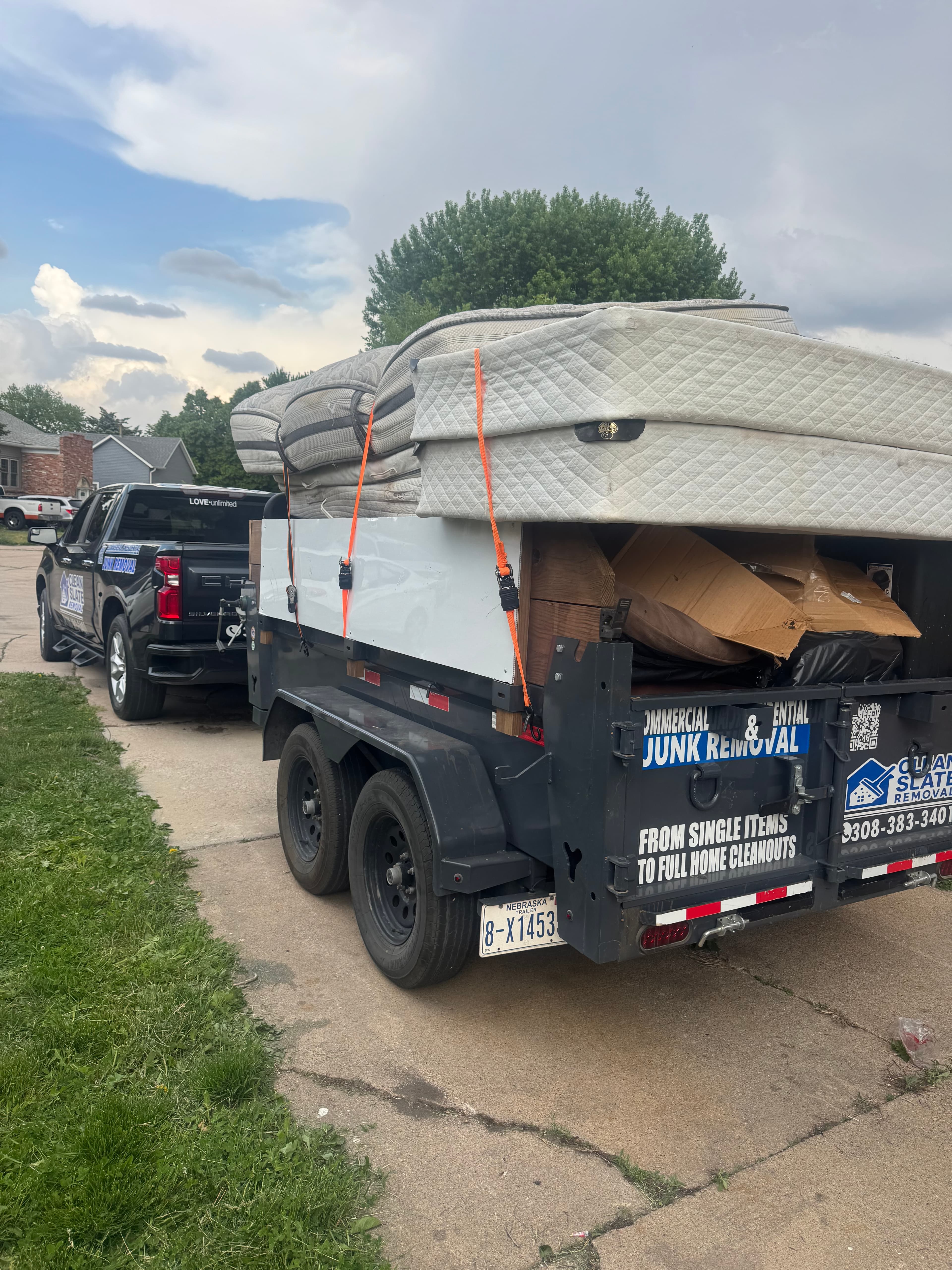 Black pickup truck towing a trailer filled with mattresses and junk on a residential driveway.