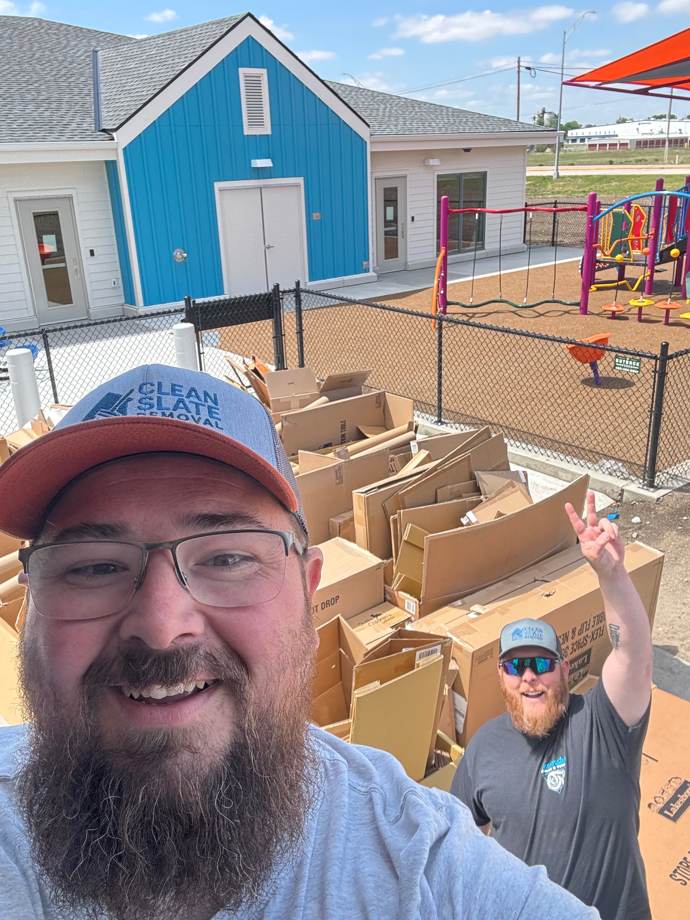Clean Slate Removal workers pose with a large pile of cardboard boxes near a playground.