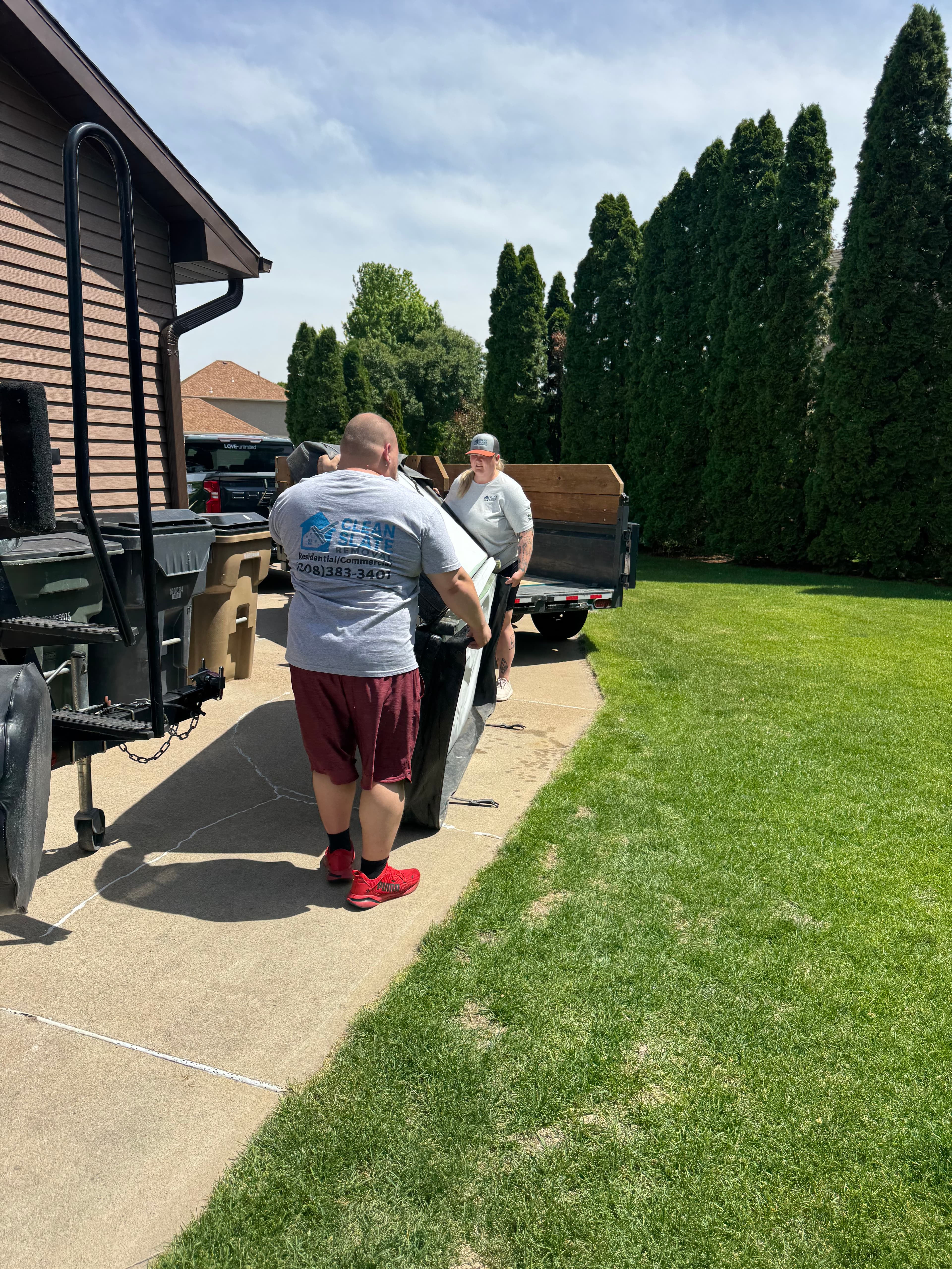 Two removal workers load a large hot tub cover onto a trailer in a driveway.