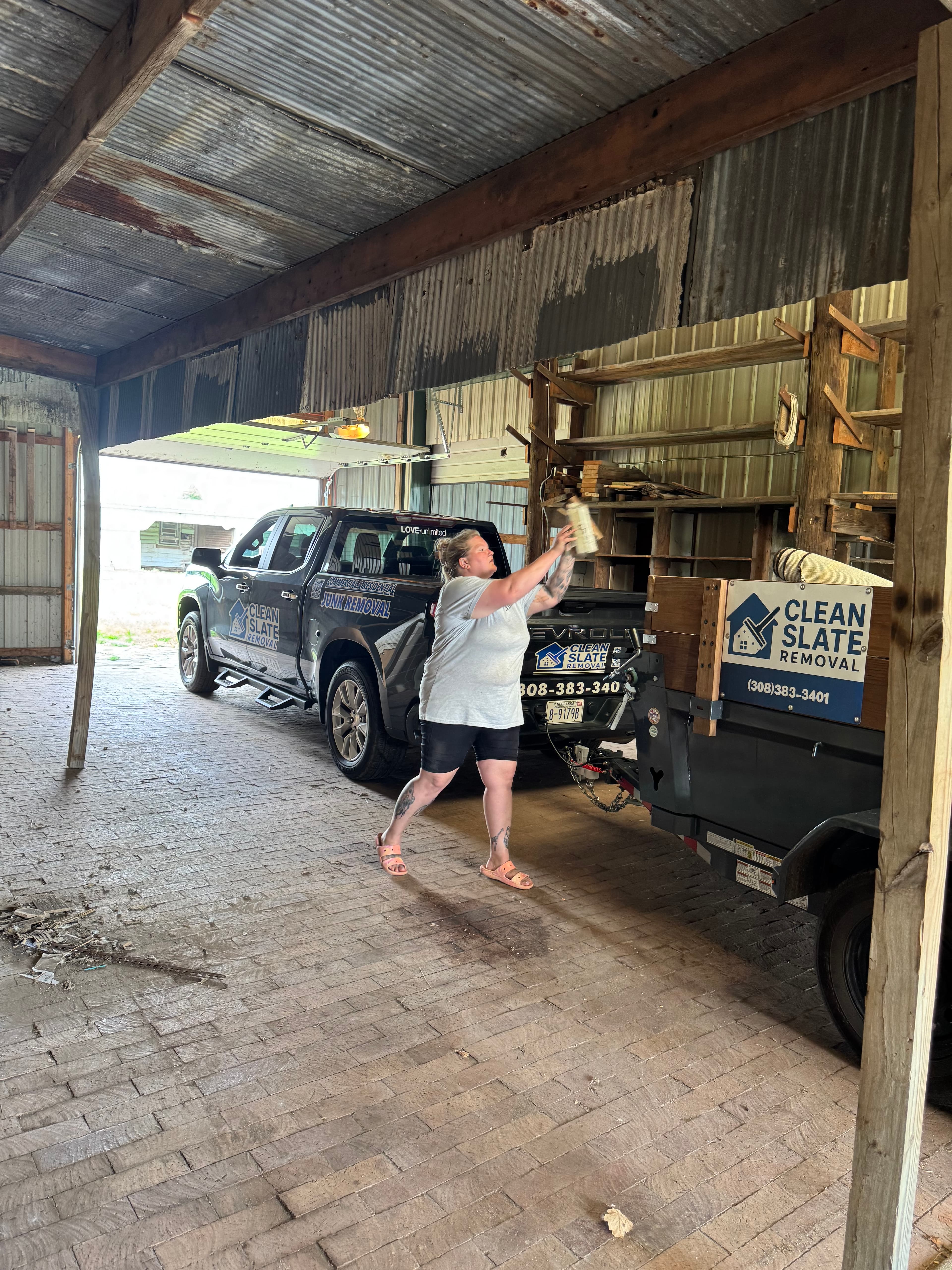 Woman loading debris into a Clean Slate Removal trailer inside a rustic brick barn.