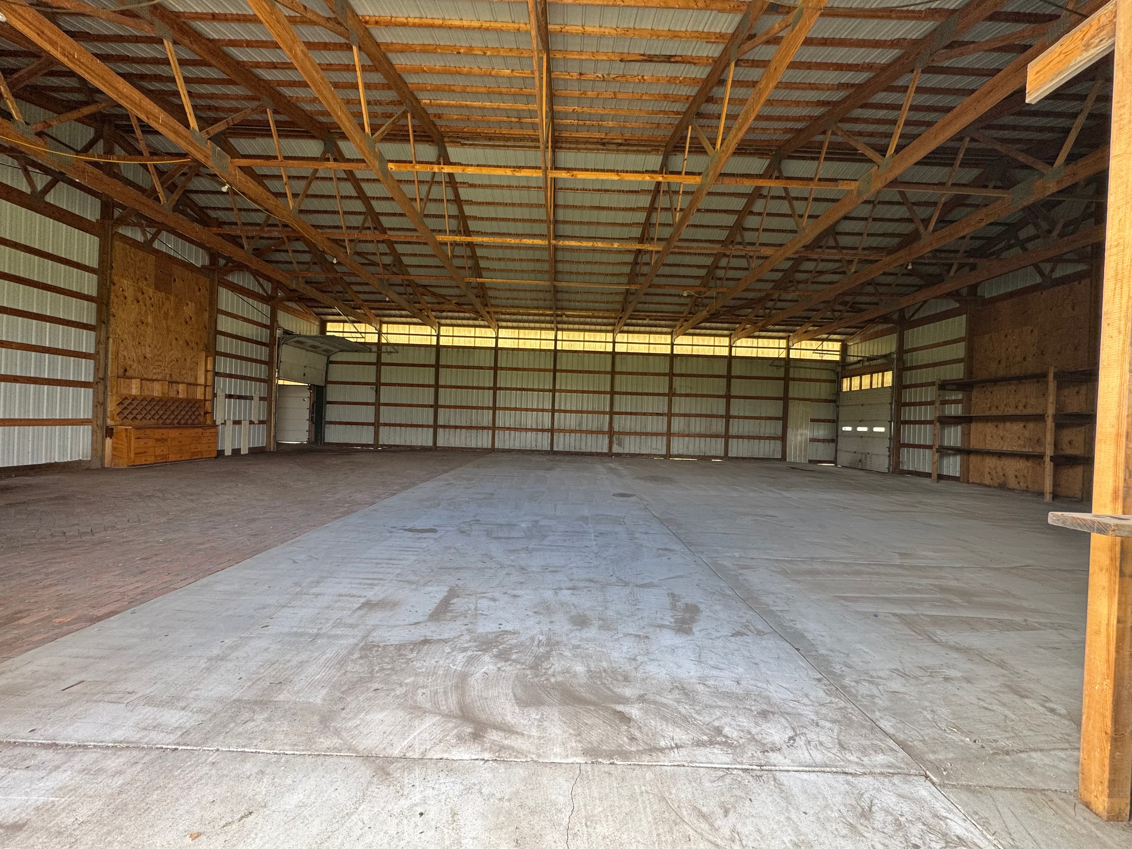 Spacious empty pole barn interior with concrete floors, metal walls, and wooden roof trusses.