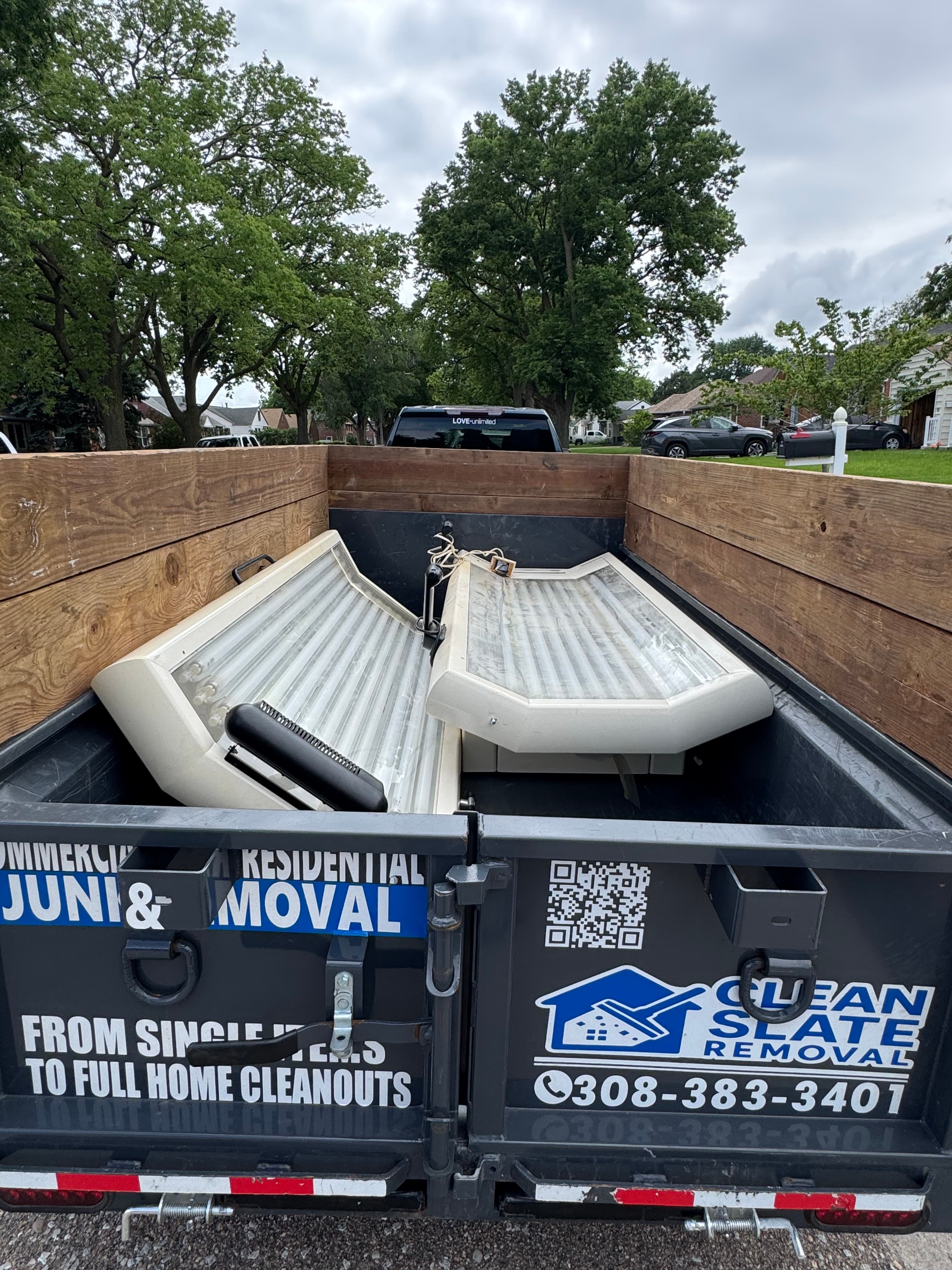 Two tanning beds inside a Clean Slate Removal trailer parked on a residential street.
