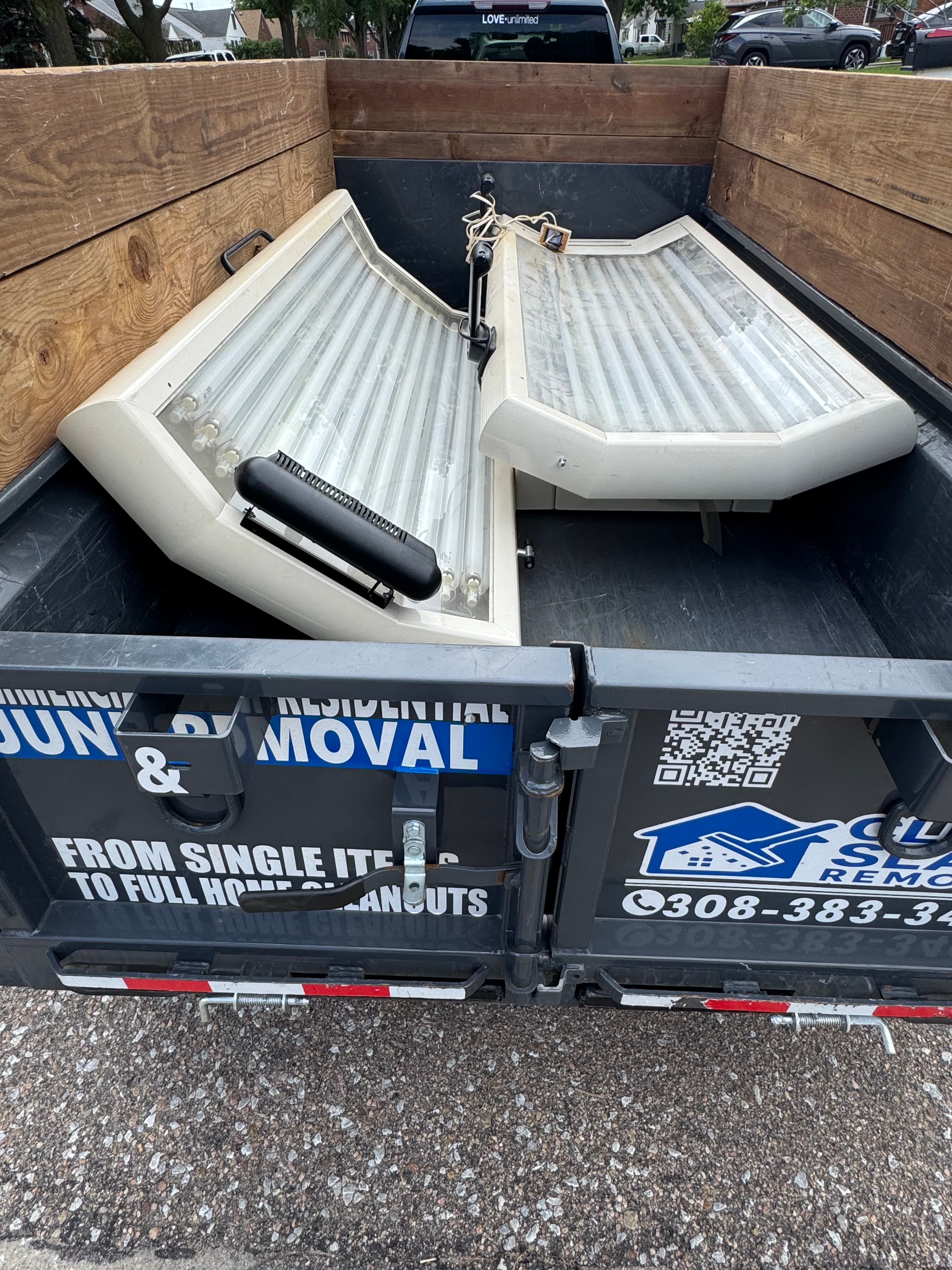 Two tanning bed panels with fluorescent tubes inside a black residential junk removal trailer.