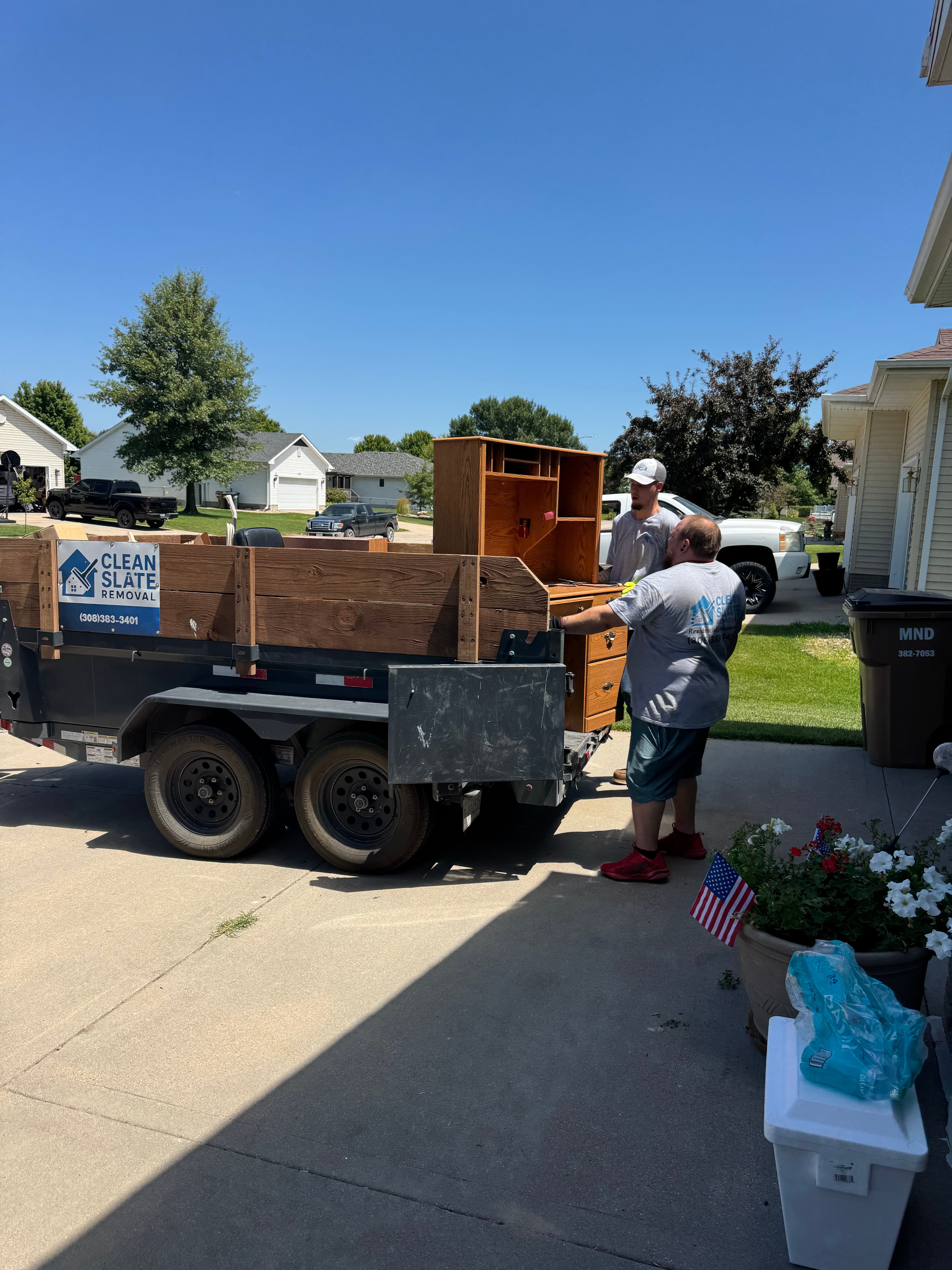 Two men loading a wooden desk onto a Clean Slate Removal trailer in a driveway.
